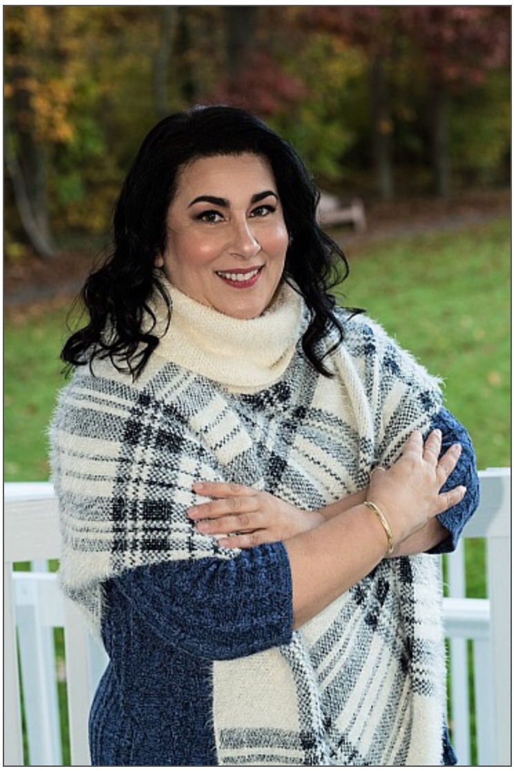 A woman standing in front of a fence wearing a sweater and scarf.